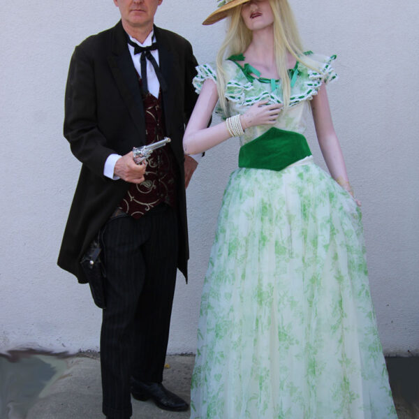 Man dress in a cowboy suite hold a fake gun and a lady mannequin in green dress.